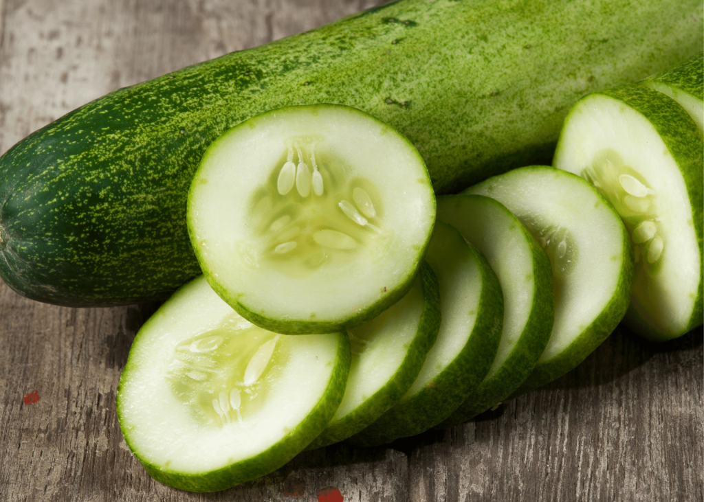 Cucumber with slices of cucumber resting  in front of it. 