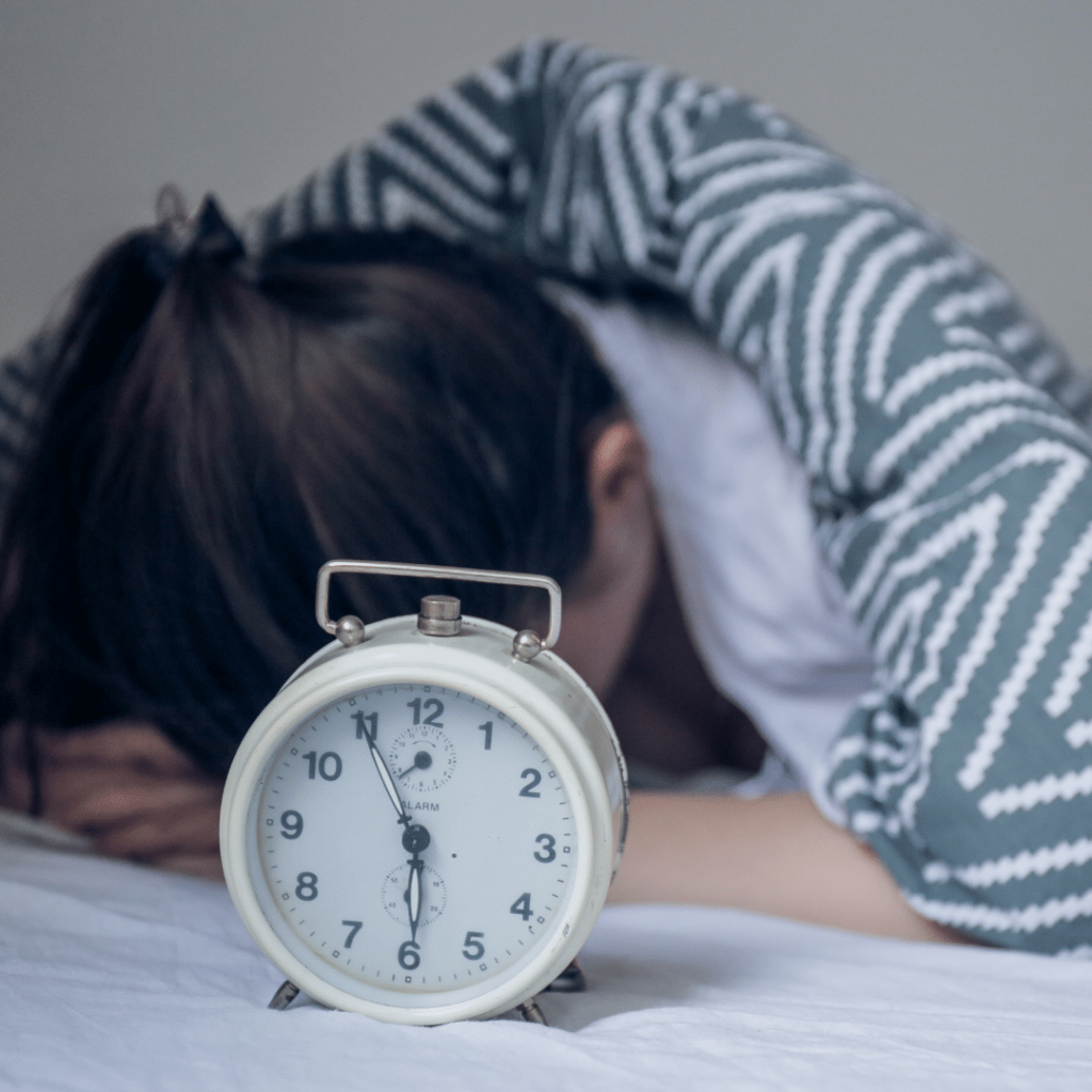 Child lying in bed with head down next to alarm clock.